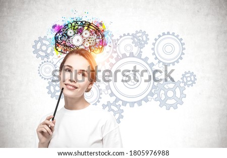 Portrait of smiling young woman with pencil standing near concrete wall with colorful brain sketch drawn on it