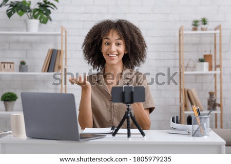 Modern hobby and blog concept. Happy african american woman looking at webcam sitting at table in interior of living room