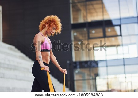 Young european redhead woman in sportive clothes doing exercises with rope outdoors.