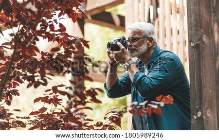 A mature man with a beard and a camera takes pictures, paparazzi. Retired active hobby, senior journalist.