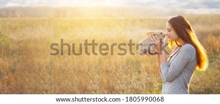 a young woman with red hair and a gray foot, Caucasian appearance, holds a cute fluffy Easter bunny in front of a stob with a place for your text, photo banner. Spring Holidays Concept