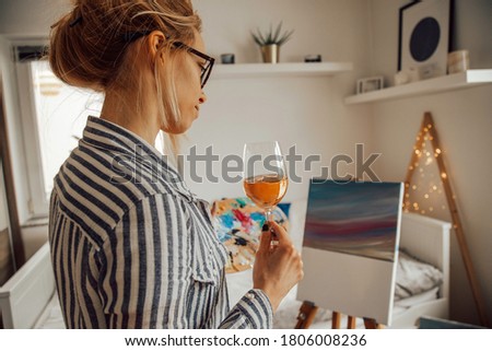 Beautiful artist woman painting in her room while drinking wine.