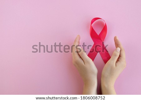 Breast cancer awareness concept. Womans hands hold pink ribbon on light background. Close up, top view