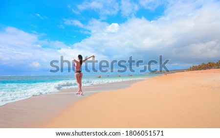 Tropical sandy beach and clear sea background with traditional balinese boats - Happy slim girl in red and black bikini with raised up arms on the seashore - Bali, Indonesia 