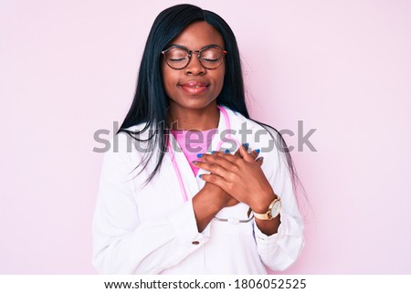 Young african american woman wearing doctor stethoscope smiling with hands on chest with closed eyes and grateful gesture on face. health concept. 