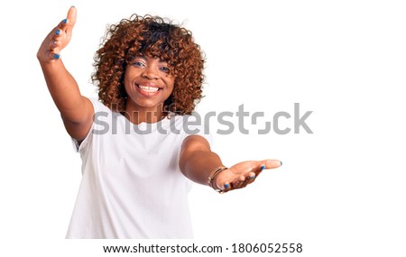Young african american woman wearing casual white tshirt looking at the camera smiling with open arms for hug. cheerful expression embracing happiness. 