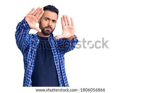 Young hispanic man wearing casual clothes doing frame using hands palms and fingers, camera perspective 