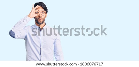 Handsome hispanic man wearing business shirt and glasses doing ok gesture shocked with surprised face, eye looking through fingers. unbelieving expression. 