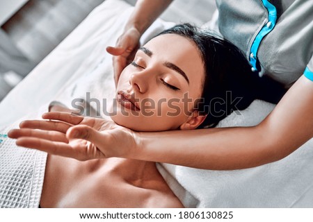Manual sculpting face massage for young woman in beauty clinic. Massage therapist is working on woman's jaw, top view. Vertical photo