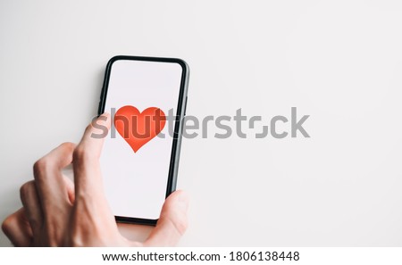 Online dating concept. Smartphone with red heart on the screen, isolated on white background. Hand touching screen