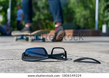 Skateboarder dropped his black glasses on the asphalt while riding the board