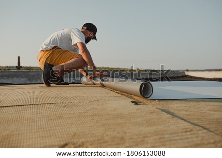 Worker applies pvc membrane roller on roof very carefully Royalty-Free Stock Photo #1806153088