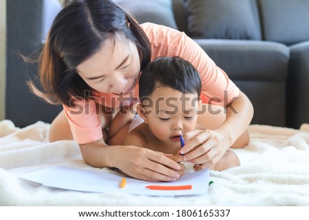 Asian mom teaching her cute baby boy to use crayons to draw on paper at home. Family and togetherness concept.