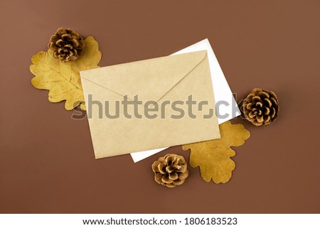 Envelope and letter, cones and dried orange leaves flat lay on brown background top view, copy space. Autumn decorations. Holidays invitations. Creative composition. Stock photo.
