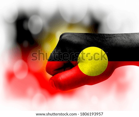 Flag of Australian Aboriginal painted on male fist, strength,power,concept of conflict. On a blurred background.