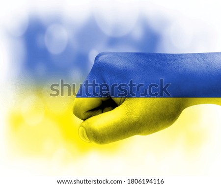 Flag of Ukraine painted on male fist, strength,power,concept of conflict. On a blurred background.