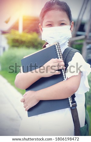 After there is a big outbreak of coronavirus everyone adjusts to new normal. little girl wearing the mask medical holding books and carry the green backpack looks happy to go to school.