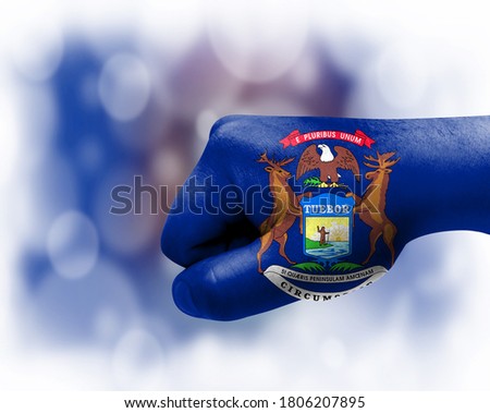 Flag of State of Michigan painted on male fist, strength,power,concept of conflict. On a blurred background.