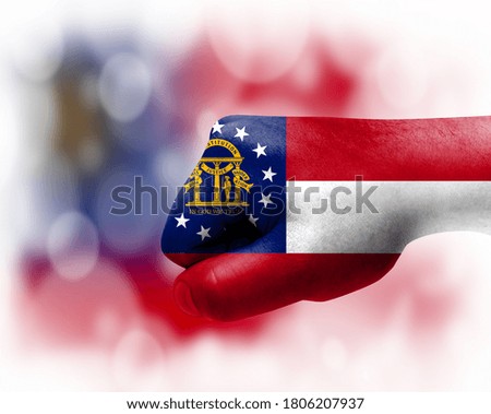 Flag of State of Georgia painted on male fist, strength,power,concept of conflict. On a blurred background.