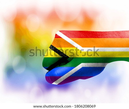 Flag of Gay pride Flag of South Africa painted on male fist, strength,power,concept of conflict. On a blurred background.