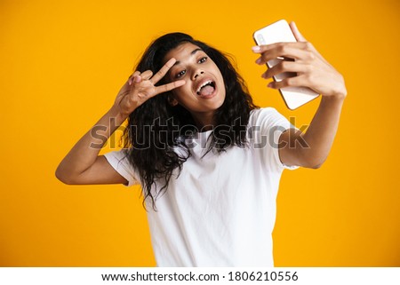 PSmiling young african woman taking selfie with mobile phone over yellow background