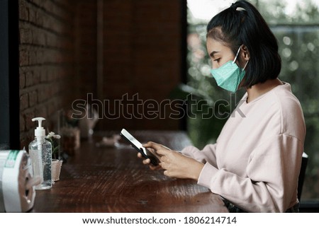 Young beautiful and cheerful woman using cellphone looking at screen with coffee and complentary on wooden table in cafe. Stock photo.