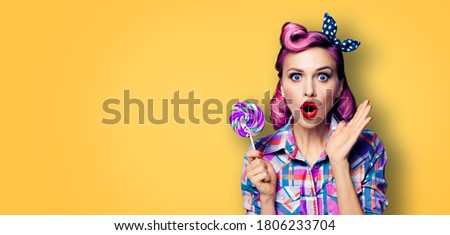 Purple head excited very surprised woman with lollipop. Pinup girl with wide opened mouth, eyes. Beauty model at retro fashion and vintage ad concept. Yellow orange color background with copy space. 