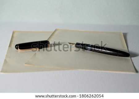 An old fountain pen with two yellowed leaves on a white surface