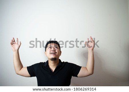 Portrait of a young Asian man Wear a black polo shirt
Doing gestures raise your hand
In a white background