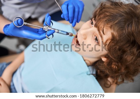 Close-up photo of a brunette boy with his mouth open getting local anesthesia for dental procedures