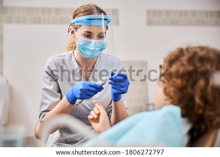Female dentist holding a syringe and getting ready to give anesthesia to the kid in a dental chair