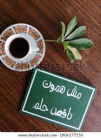 Motivational Arabic quote closeup coffee and green leaves on wooden background.