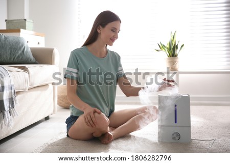 Woman near modern air humidifier at home Royalty-Free Stock Photo #1806282796