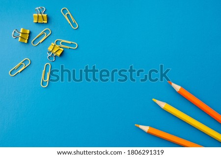 Orange and yellow pencils with paper clips on a blue background, flat lay. Blank copy space