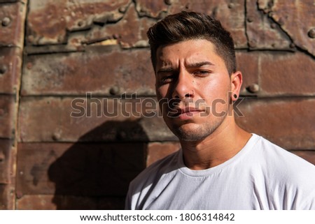 Man with an intense look on a rusty background, white T-shirt and black earring