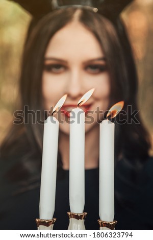 Vertical portrait of dark hair straight hairstyle witch voodoo black horns head woman hold hand three candles holder flame selective focus autumn holiday horror scary festival party halloween concept