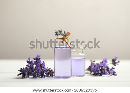 Bottles of essential oil and lavender flowers on white wooden table