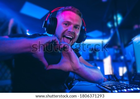 Happy professional cyber sport gamer playing online computer game with headphones, Blurred Red and Blue background.