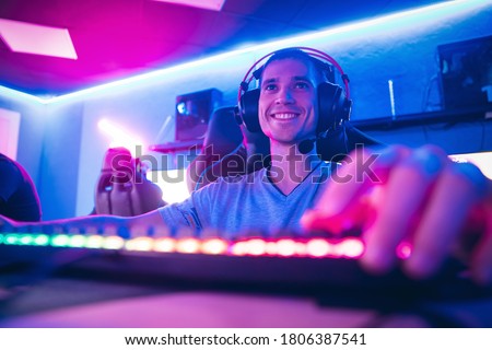 Happy professional cyber sport gamer playing online computer game with headphones, Blurred Red and Blue background.