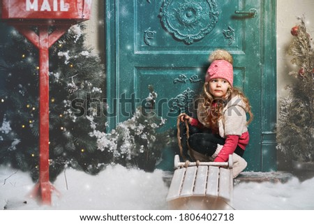 cute little girl sitting near the door of the house on Christmas evening. child walks down the street with a sled alone