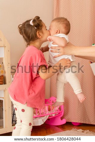 Lifestyle portrait of happy family: toddler girl and baby boy hug and kiss each other at home. Cheerful family: brother and sister smile and have fun in nursery room Brotherhood and sisterhood concept