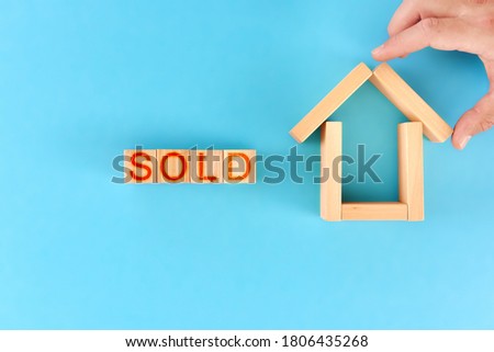 sold. a man builds a house from wooden blocks next to the sign sold