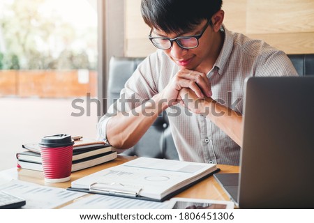 Asian man write a report and using laptop computer working on his new project idea in cafe.