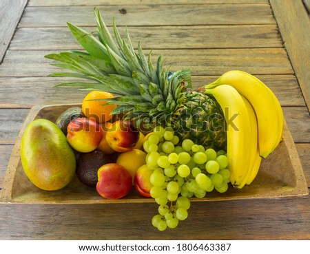 Wooden bowl full of fruit, bananas, pineapple, grapes, mango, nectarines