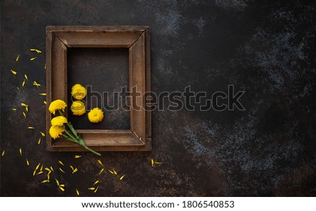 Old wooden frame with autumn flowers and leaves on brown rustic wooden background. Autumn flowers composition with copy space.