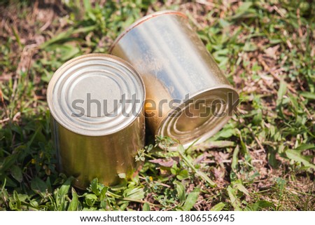 Two closed metal cans are on the forest ground. Close-up photo