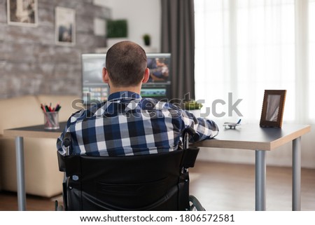 Video editor in wheelchair working on film post production. Invalid videographer doing his business online, using high technology, sitting in his apartment, working remotely in special conditions.