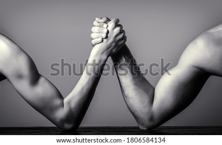 Two man's hands clasped arm wrestling, strong and weak, unequal match. Arm wrestling. Heavily muscled man arm wrestling a puny weak man. Black and white.
