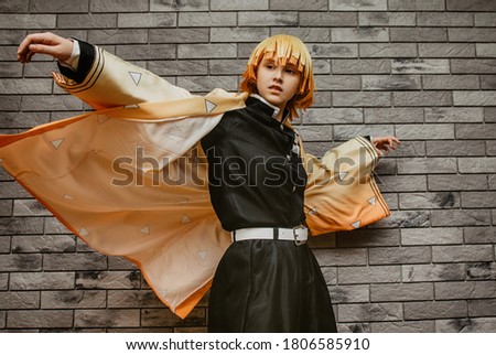 portrait of a teenage girl with yellow hair in an anime hero costume on a gray wall background