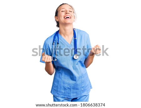 Young beautiful blonde woman wearing doctor uniform and stethoscope very happy and excited doing winner gesture with arms raised, smiling and screaming for success. celebration concept. 